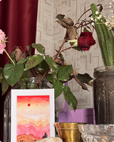 Pink layered mountain sunset postcard among rose stems and a cactus