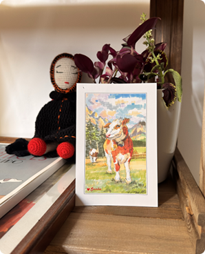 Standing card of a brown-and-white calf in an alpine meadow propped on a shelf