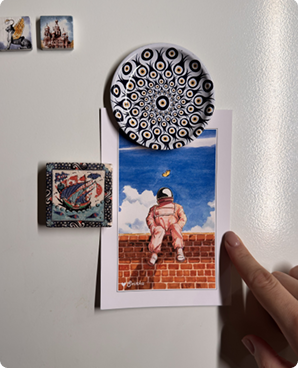 Whimsical astronaut-on-a-brick-wall postcard held on a fridge by magnets