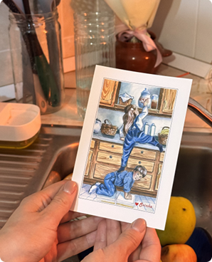 Hand-drawn postcard of blue cartoon cats busy in a vintage kitchen, held in hands