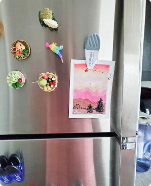 Pink sunset mountain postcard with pine trees clipped to a fridge