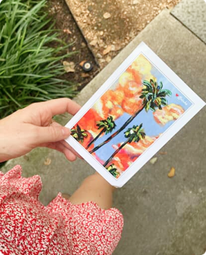 Bright postcard of palm trees and seaside houses held outdoors on a path